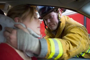 Firefighter Assisting A Woman With A Neck Brace After A Car Accident Injury, Highlighting Emergency Response And Care For Vehicle Accident Victims.