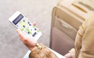 A Person Holding A Smartphone Displaying A Rideshare App Interface With A Map And Ride Options, Sitting Next To A Suitcase, Symbolizing The Need For A Duncanville Rideshare Accident Lawyer.